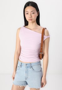 Top de un hombro en púrpura claro, hecho de una tela suave y elástica, combinado con pantalones cortos de mezclilla azul claro con dobladillos deshilachados y bolsillos frontales.