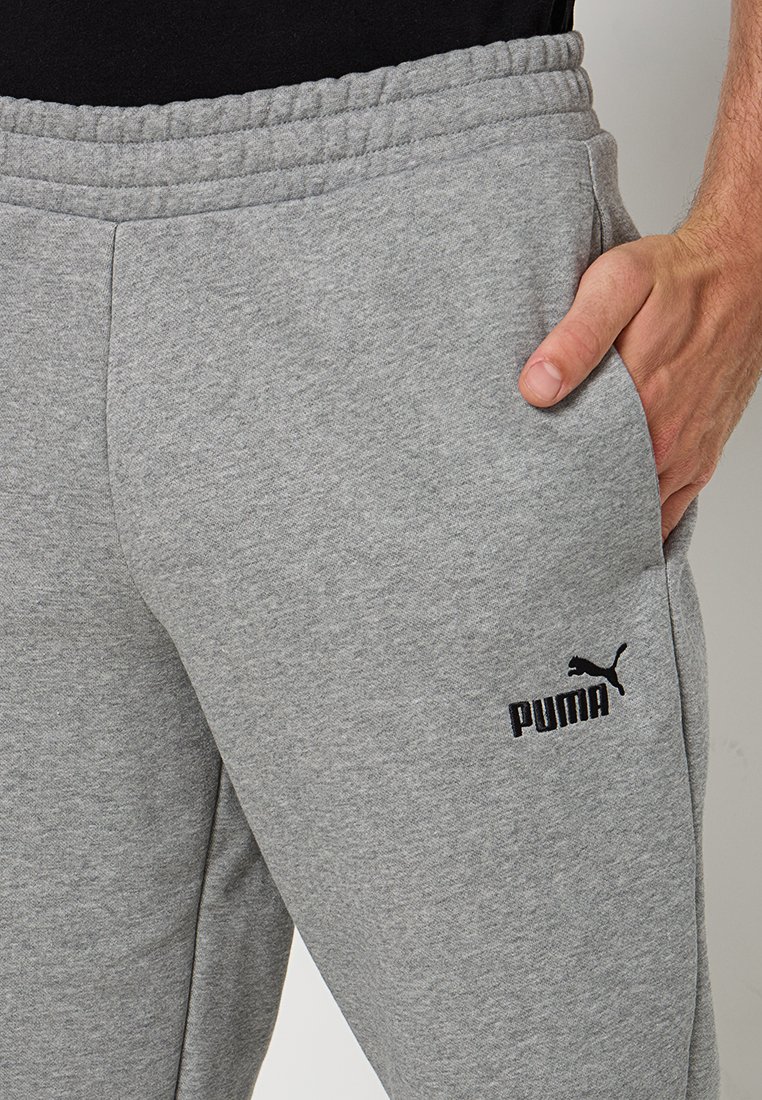 Pantalon de survêtement gris avec une texture douce, taille élastique, poches latérales et un logo Puma noir sur la cuisse gauche.