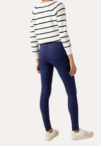 Jeans skinny azul marino con bolsillos traseros, combinados con un suéter de punto blanco y negro a rayas, con mangas ajustadas. Zapatillas blancas.
