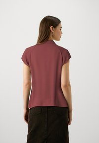Short-sleeve, burgundy blouse with a collar, smooth fabric, and a slightly flared hem, paired with a dark denim skirt.