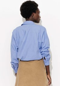 Chemise bleu clair avec un col boutonné, des manches longues et une coupe décontractée, assortie à une jupe beige en tissu doux.