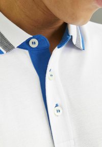 Poloshirt in Weiß mit blauen Akzenten am Kragen. Verfügt über einen strukturierten Strickstoff und mehrere Knöpfe, mit einem kontrastierenden karierten Muster.