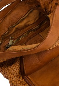 Tan leather handbag interior with a woven texture, featuring a zippered pocket, smooth lining, and visible branding.