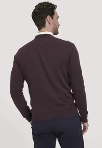 Bordeauxfarbener Strickpullover mit rundem Ausschnitt und gerippten Bündchen und Saum. Die Textur wirkt glatt mit einem figurbetonten Design.