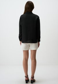 Maglietta nera a maniche lunghe con vestibilità comoda, realizzata in tessuto leggero, abbinata a pantaloni corti bianchi e tacchi neri con cinturini.