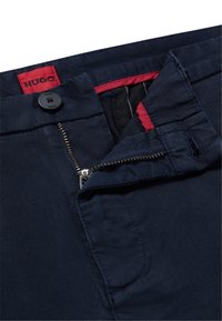 Navy blue pants featuring a zip fly and button closure. The interior waistband has red accents; includes a visible logo tag. Smooth texture.