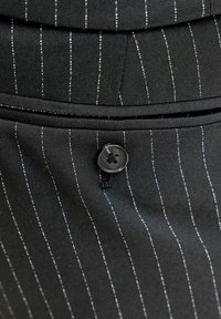 Czarna tkanina z białymi prążkami, z czarnym guzikiem i przeszyciami. Tekstura wydaje się gładka z uporządkowanymi elementami wzorniczymi.