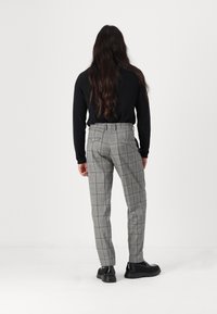 Pantaloni gri cu carouri, cu o croială adaptată, având o textură netedă, două buzunare la spate și asortați cu un top negru cu mâneci lungi și încălțăminte neagră.