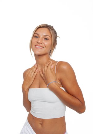 Weißes Cropped Top mit dünnen Trägern, glatter Stoff, der eine durchtrainierte Figur zur Schau stellt. Armband mit blauen Akzenten, am Handgelenk getragen. Neutraler Hintergrund.