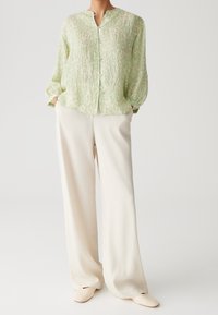 Blusa verde chiaro, con texture, davanti con bottoni e colletto alla mandarina. Abbinata a pantaloni larghi color crema e scarpe slip-on.