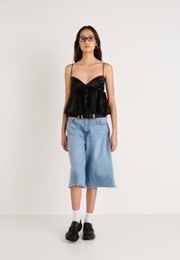 Czarny satynowy top z baskinką na cienkich ramiączkach, zestawiony z jasnoniebieskimi szerokimi spodnicami culottes z denimu. Modelka nosi czarne buty i białe skarpetki.