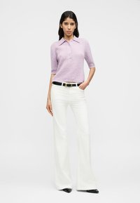 Λιλά κοντομάνικο πλεκτό πουλόβερ πόλο με κουμπιά, συνδυασμένο με λευκό καμπάνα παντελόνι και μαύρη ζώνη. Μαύρα παπούτσια με μυτερή μύτη ολοκληρώνουν το σύνολο.