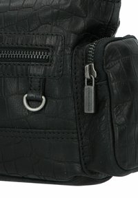 Sac en cuir noir avec une texture crocodile, présentant un compartiment zippé, un détail en forme d'anneau en métal et des accents en métal.