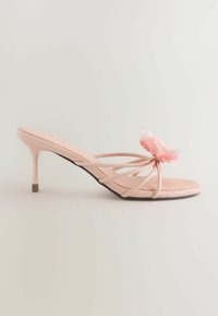 Różowa sandałka na obcasie ze smukłym szpilkowym obcasem i dekoracyjnym różowym kwiatem na pasku z przodu, na jednolitym tle.