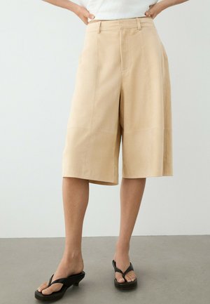 Shorts beiges larges longueur genoux portés avec des sandales noires à talons et un top blanc, présentés sur une personne debout.