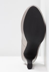 Chaussure à talon haut beige élégante avec une surface extérieure lisse et brillante en cuir, dotée d'une semelle en caoutchouc noire texturée. Conception à bout arrondi.