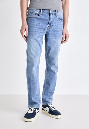 Jeans in denim azzurro chiaro con taglio dritto, design classico a cinque tasche e leggera sfumatura. Abbinati a sneakers navy con dettagli bianchi.