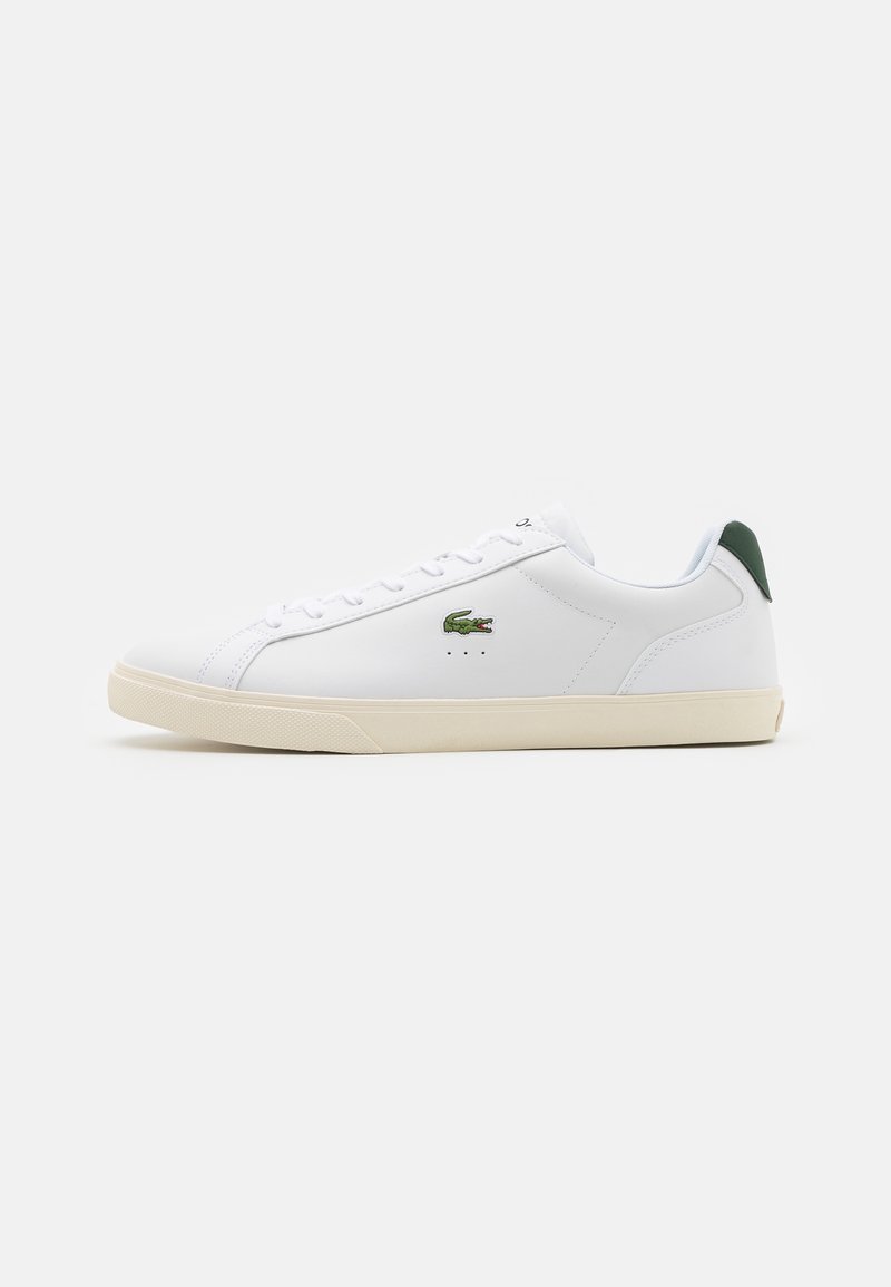 Baskets en cuir blanc avec une semelle en caoutchouc crème, un accent vert au talon, et un petit logo crocodile brodé sur le côté.