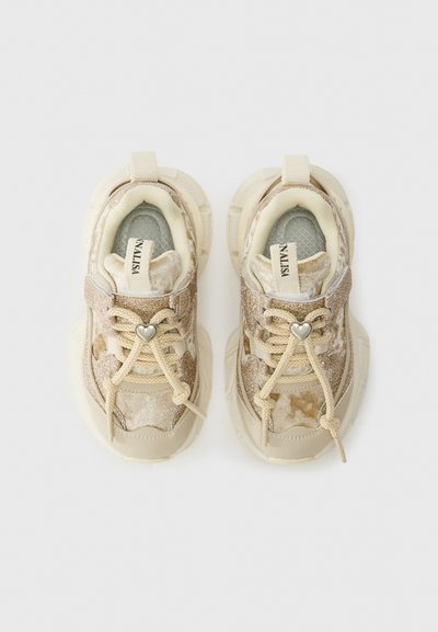 Beige Kleinkinder-Sneaker mit samtiger Textur, glitzernden Akzenten, cremefarbenen Schnürsenkeln, die mit silbernen herzförmigen Charms gebunden sind, und Zuglaschen auf weißem Hintergrund.