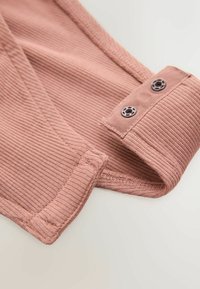 Dusty rose ribbed fabric with a soft texture, featuring a folded hem and two dark buttons for closure on the edge.