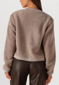 Bruine fleece jas met een zachte, getextureerde afwerking, een cropped ontwerp en een geribbelde zoom. Heeft lange mouwen en een ronde halslijn.