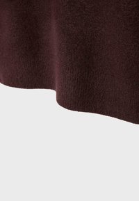 Tissu tricoté brun foncé avec une texture douce et duveteuse et un bord légèrement incurvé sur un fond clair.