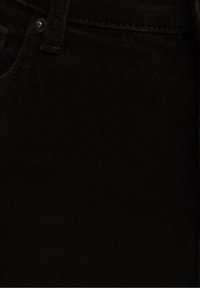 Primer plano de una tela de mezclilla negra mostrando un bolsillo frontal, costuras y un remache metálico en la cinturilla.