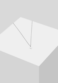 Silver necklace with a thin chain and a small, intricate flower-shaped pendant on a light gray display surface.