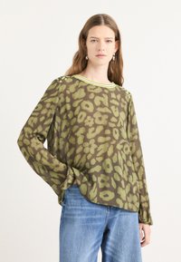 Doorzichtig blouse met lange mouwen en een groen luipaardprint op een bruine achtergrond. Voorzien van een ronde halslijn met een felgele afwerking.