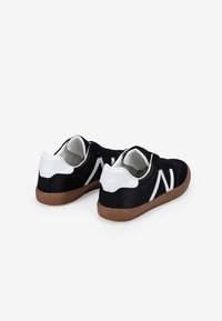 Sneakers neri in tela con accenti bianchi e suola in gomma marrone. Presentano un design classico, allacciatura frontale e una leggera texture sulla parte superiore.