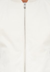 Casaco bomber branco com uma textura suave, apresentando um fecho de correr central, gola canelada e bolsos laterais. Design simples sem padrões visíveis.