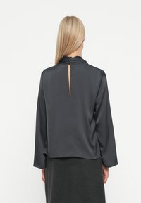 Blusa di raso grigio scuro con maniche lunghe e dettaglio a scollatura a chiave sul retro, caratterizzata da una consistenza morbida e una vestibilità ampia e rilassata.