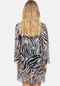 Przezroczysta sukienka w biało-czarny zebrzy wzór z długimi rękawami, luźnym krojem i długością do połowy uda, prezentująca gładką, przezroczystą fakturę.