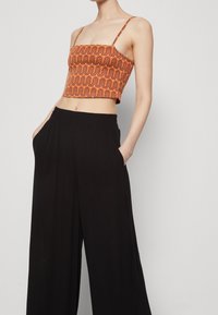 Cropped top with orange wave pattern and thin straps, paired with black wide-leg trousers featuring side pockets and elastic waistband.