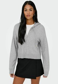 Hallhalli hall, mis on valmistatud pehmest kangast. Ees lukuga, ribatreppide äärega käised ja alläär, ning reguleeritav nööriga kapuuts. Koos musta seelikuga.