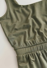 Ärmelloses olivgrünes Kleid mit gerafftem elastischen Bund, flach auf einem hellen Hintergrund präsentiert, mit sichtbarer Stofftextur und Nähtem.