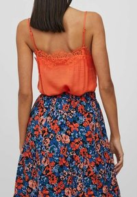 Orange cami med spetsdetaljer i kanterna, ihopparad med en blommig kjol med röda, blåa och gröna mönster. Justerbara spaghetti-bärs.