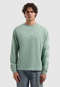 Mintgroen shirt met lange mouwen en een ronde hals, met witte bedrukte tekst en logo's op beide mouwen. Gemaakt van zacht katoen.