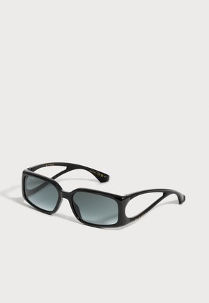 Lunettes de soleil rectangulaires noires avec branches découpées et verres teintés foncés, présentées sur un fond clair uni.