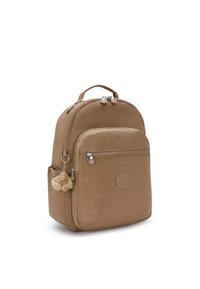 Mochila de tela marrón con un diseño redondeado, compartimentos con cremallera y un charm peludo colgando del tirador de la cremallera frontal.