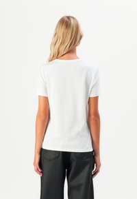 T-shirt bianco a maniche corte in cotone, con scollatura rotonda e vestibilità standard, abbinato a pantaloni neri a gamba larga.