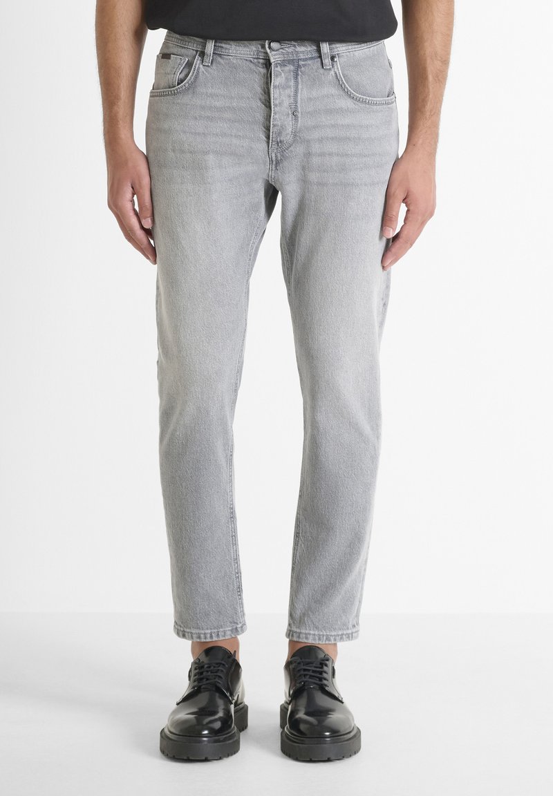 Jeans de denim gris claro con un diseño de pierna recta, cinco bolsillos y detalles de costura visibles. Llevados con zapatos negros de cordones.