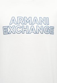 Λευκό ύφασμα με μεγάλα γράμματα τύπου block με μπλε περίγραμμα που σχηματίζουν τη φράση «ARMANI EXCHANGE» σε δύο καμπυλωτές γραμμές.