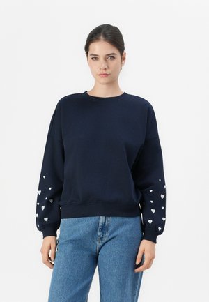 Navy sweatshirt with long sleeves, round neckline, and ribbed cuffs. Accents of white heart patterns on sleeves. Soft fabric, relaxed fit.