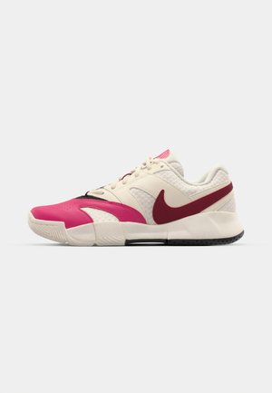 Nike sneakers feature a blend of light beige mesh and pink leather accents, with a purple heel tab and black rubber sole for traction.