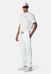 Camiseta blanca de algodón con el logo "NORTH SAILS", combinada con pantalones de chándal blancos con cordón y marca a juego. Zapatillas blancas.