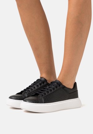 Baskets noires avec motif texturé et bout rond. Elles possèdent une semelle blanche plate et des lacets noirs. Fabriquées en matériau synthétique, design bas.