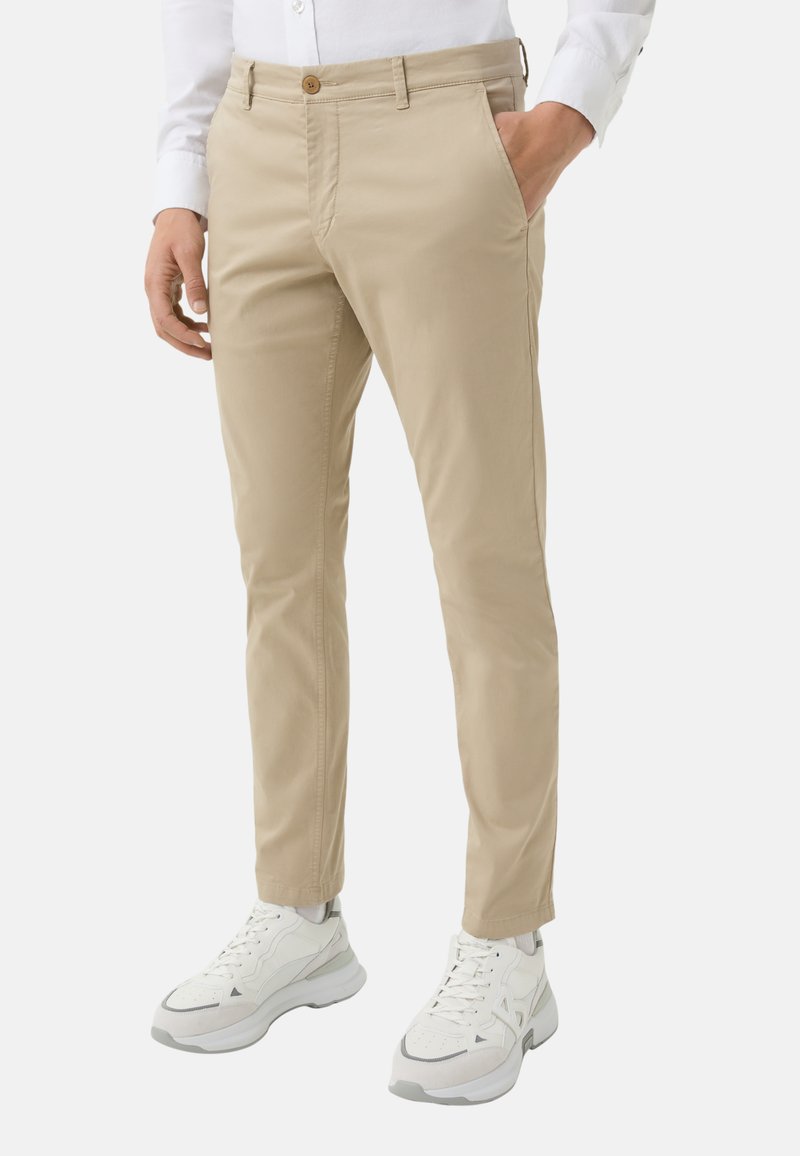 Beige cotton chinos with a straight fit and a button closure, featuring side pockets and a smooth texture, paired with white athletic sneakers.