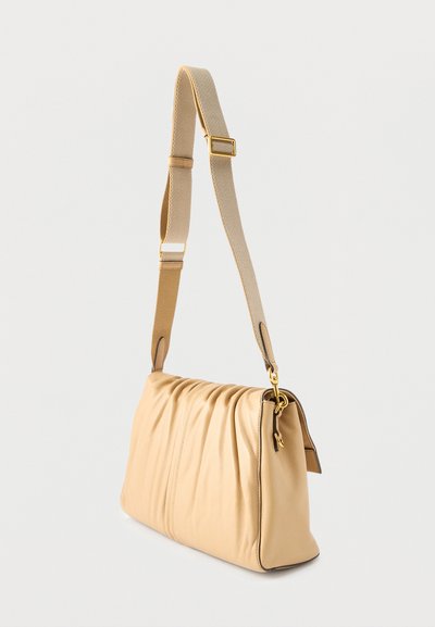 Μπεζ δερμάτινη τσάντα ώμου με χρυσά μεταλλικά στοιχεία και ρυθμιζόμενο πλεκτό λουρί σε λευκό φόντο.