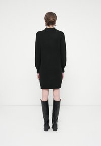 Melnas adītas kleitas ar garām piedurknēm, pieguļoša silueta un ribota apkakle. Stilizēta ar ceļgala augstuma melniem ādas zābakiem.